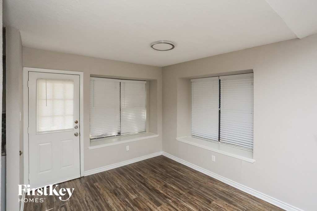 A room with a white door, two windows with blinds, and wooden flooring.