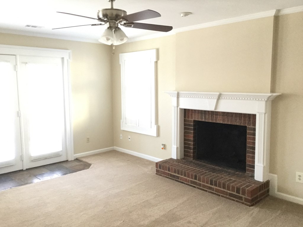 an empty living room with a brick fireplace and a ceiling fan