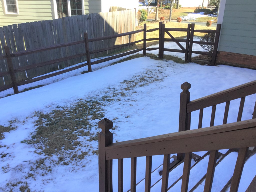 a yard covered in snow with a wooden fence