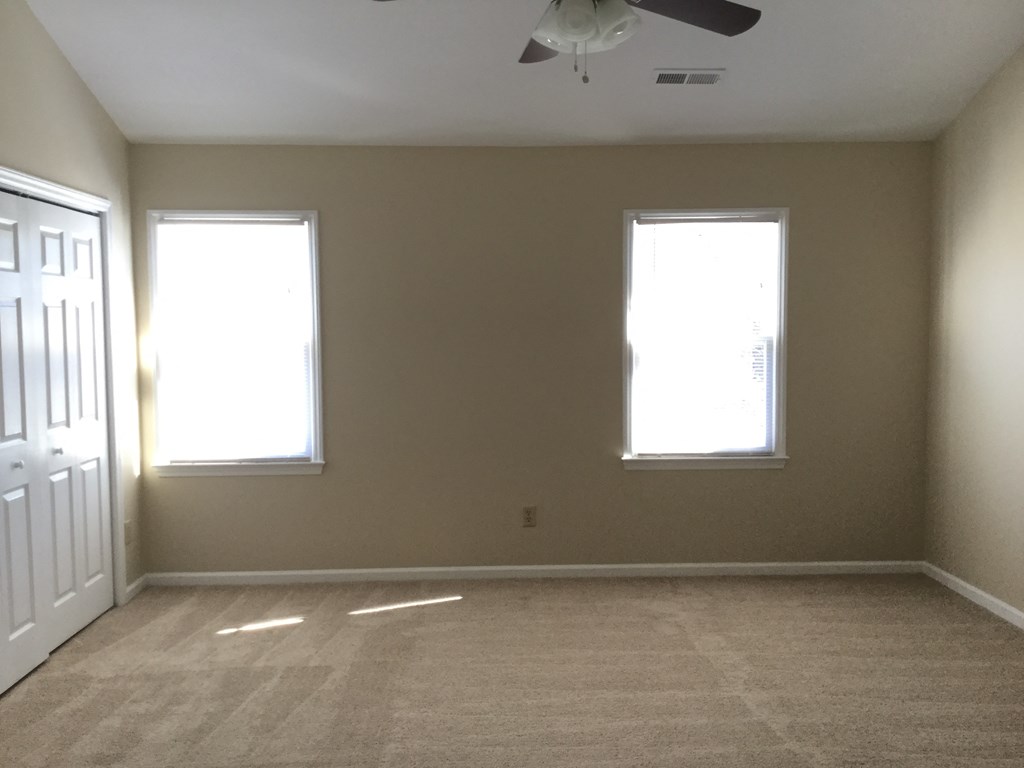 an empty room with two windows and a ceiling fan