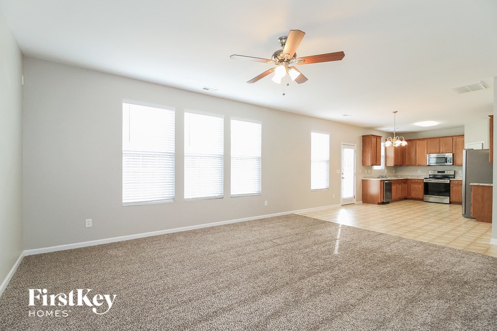 A spacious living room with a fan and a kitchen in the background.