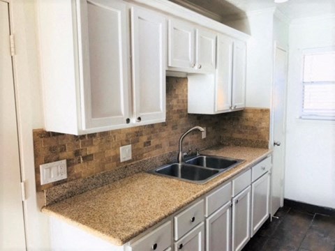 A kitchen with white cabinets and a brown tile backsplash.