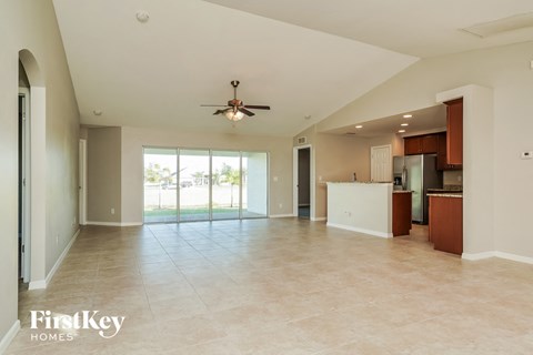 an empty living room with a kitchen and a ceiling fan