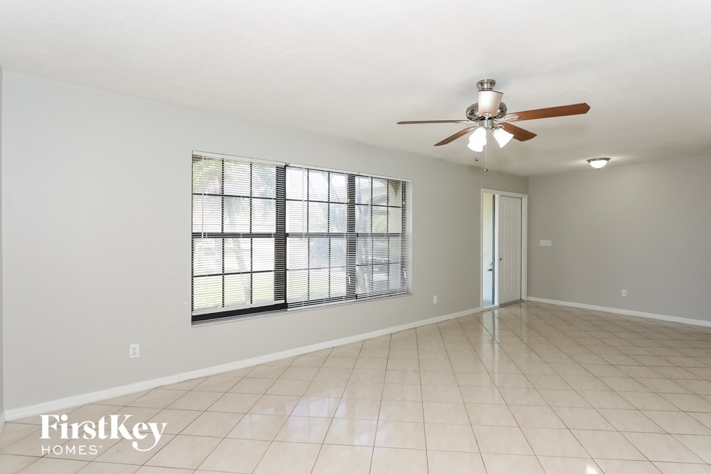 an empty living room with a large window and a ceiling fan