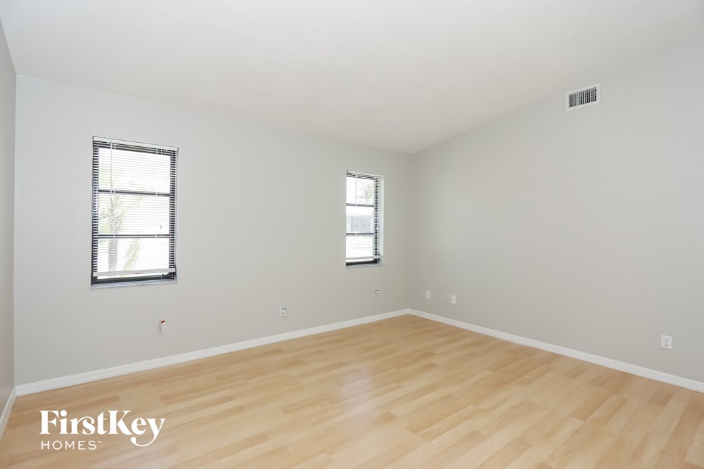 a spacious living room with wood flooring and two windows