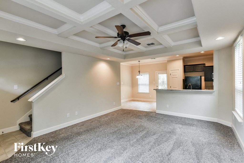 A spacious room with a ceiling fan and a staircase on the left side.