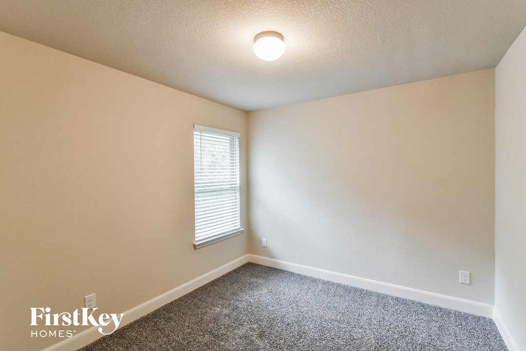 A room with a carpeted floor, a window with blinds, and a light fixture on the ceiling.