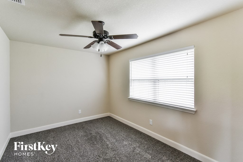 A room with a ceiling fan, carpeted floor, and a window with blinds.