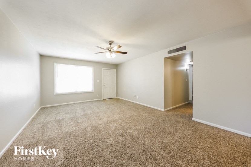 a spacious living room with carpet and a ceiling fan