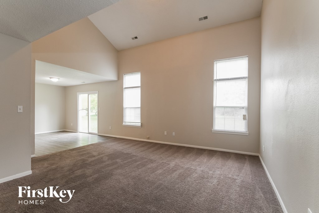 A spacious room with carpet flooring and two windows.