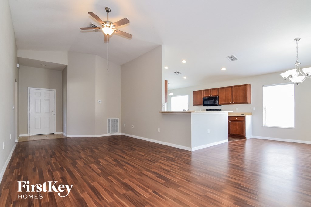 an empty living room with wood flooring and a kitchen