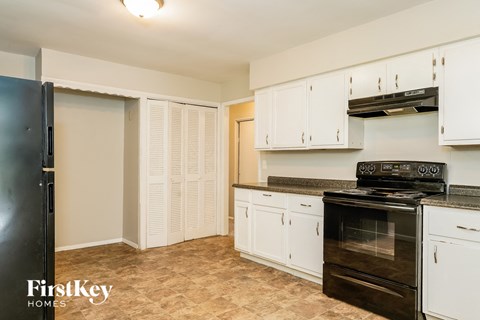 A kitchen with a black fridge, black stove and white cabinets.