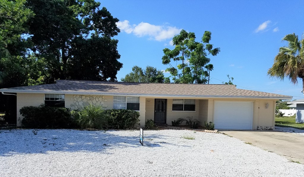 a white house with a gravel driveway and palm trees