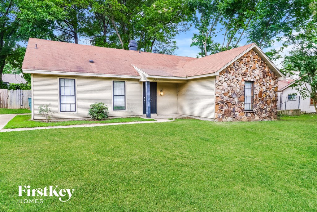 a small white house with a grassy yard and a stone house
