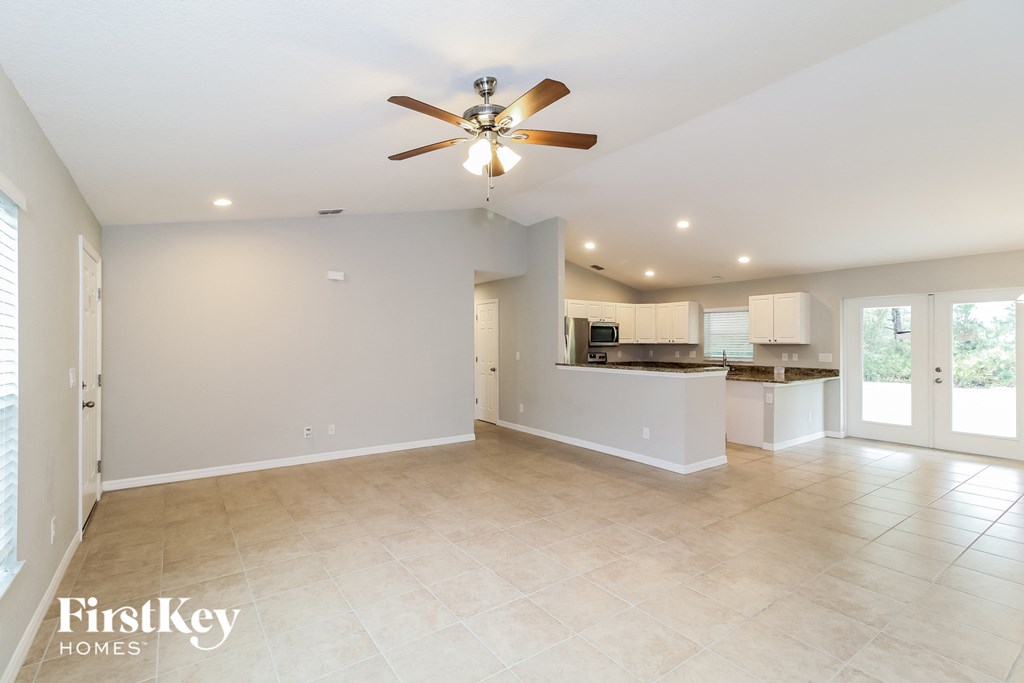 an empty living room with a ceiling fan and a kitchen
