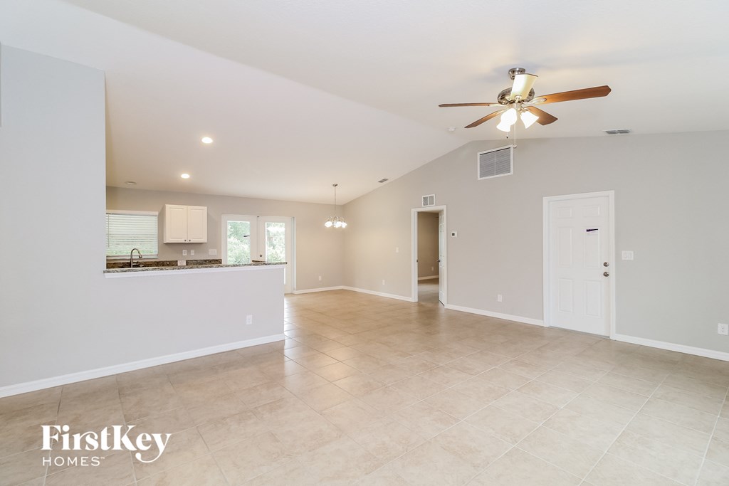 an empty living room with a ceiling fan and a kitchen