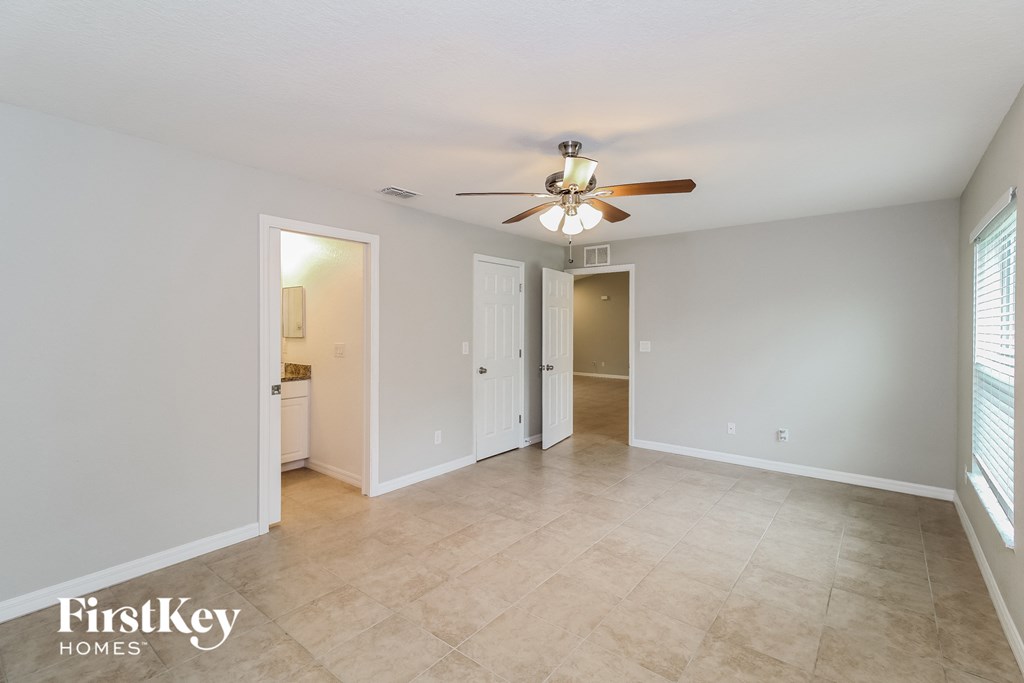an empty living room with a ceiling fan and a door to a kitchen