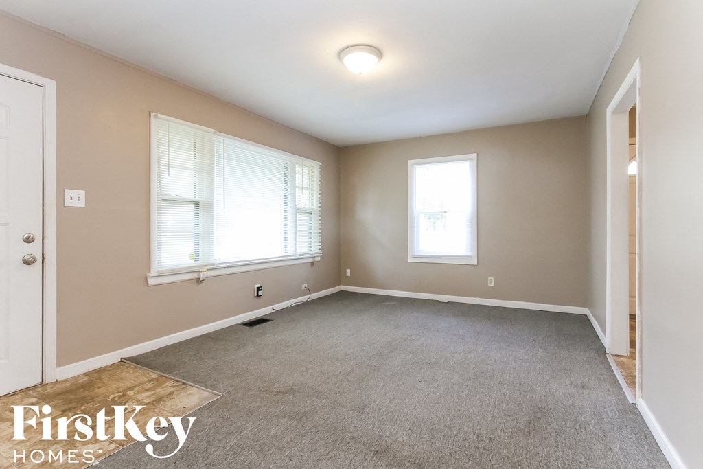 an empty living room with a carpeted floor and two windows