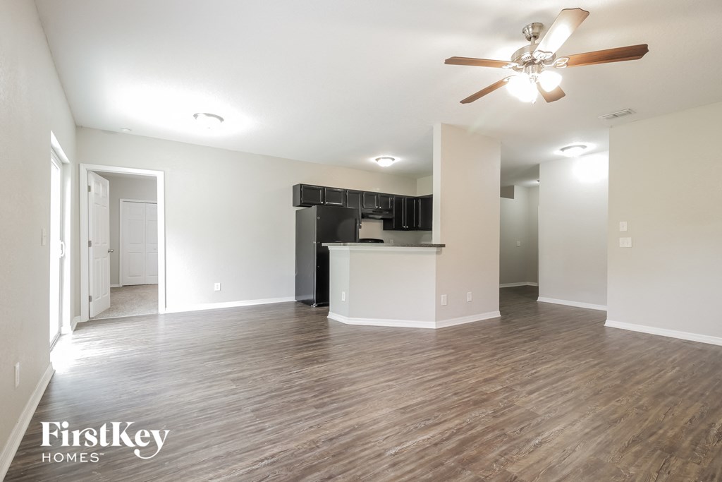 an empty living room with a ceiling fan and a kitchen