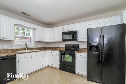 A black refrigerator stands in a kitchen with white cabinets and a granite countertop.