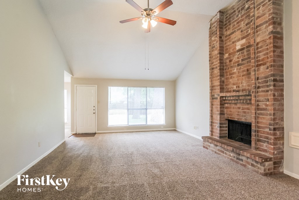 an empty living room with a brick fireplace and a ceiling fan