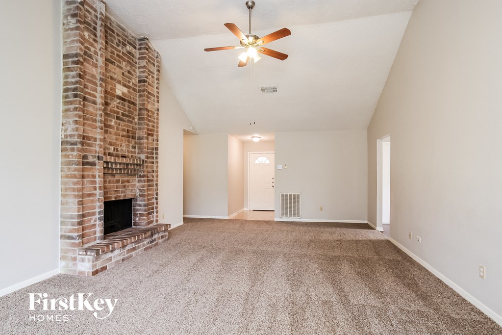 an empty living room with a brick fireplace and a ceiling fan