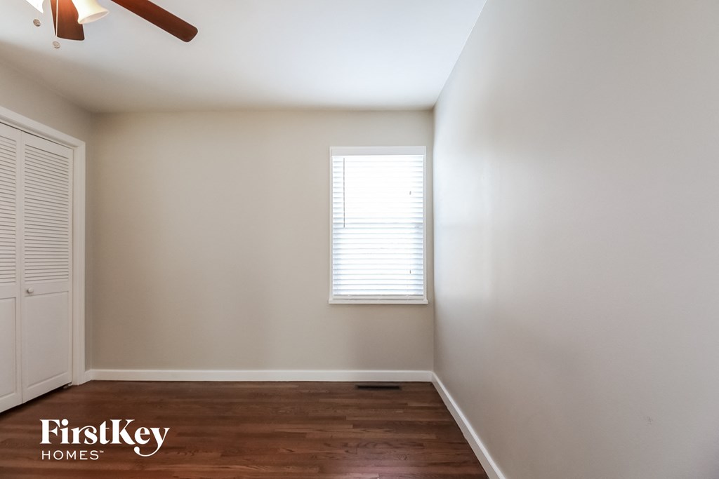 a bedroom with white walls and wood floors and a window