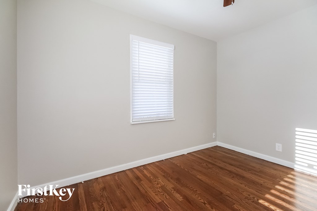 a bedroom with white walls and wood floors and a window