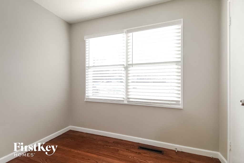 a bedroom with wood floors and a window with white shutters