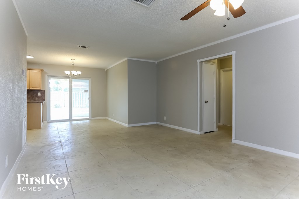 an empty living room with a ceiling fan and a door to a kitchen