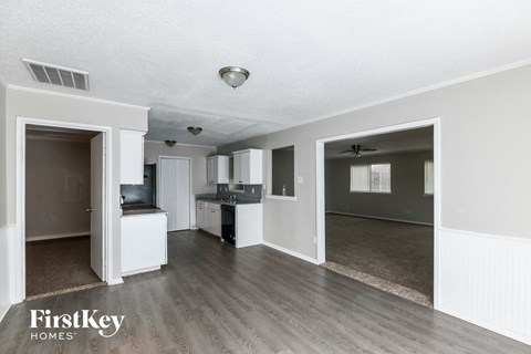 A spacious living room with a kitchen in the background and a doorway leading to another room.