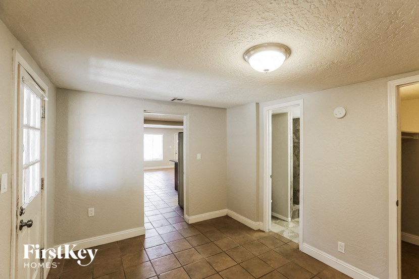 an empty living room with tile flooring and a door to a hallway