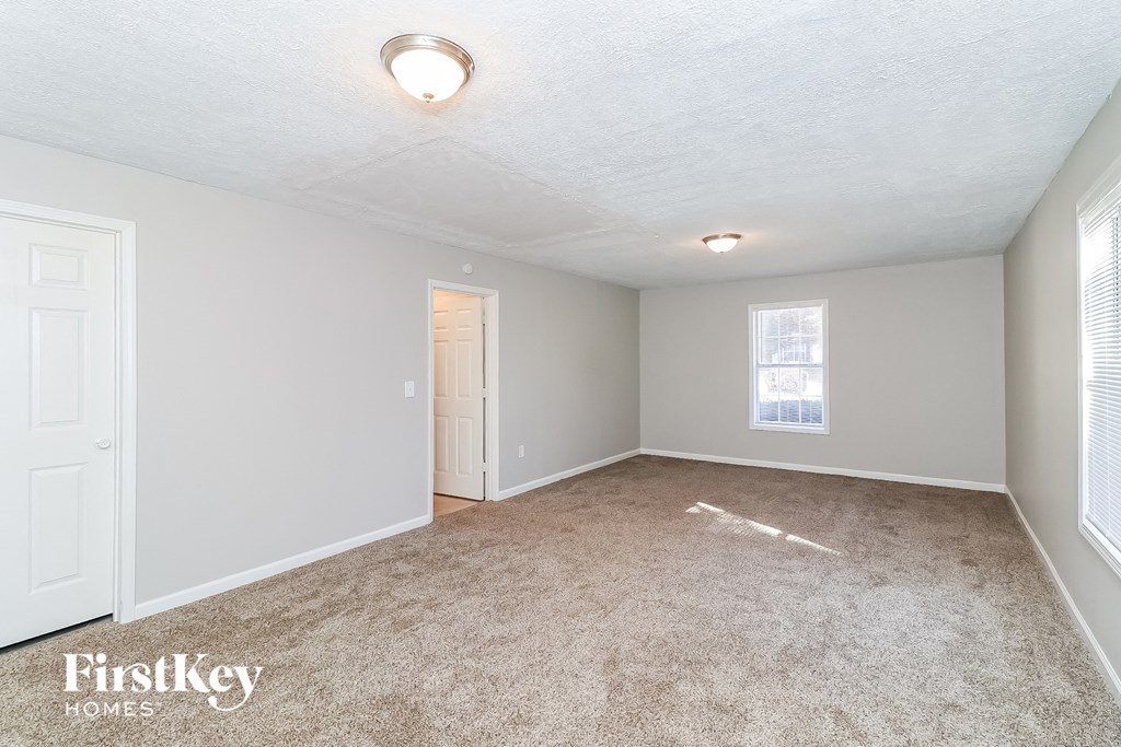 a spacious living room with carpet and a door to a bedroom