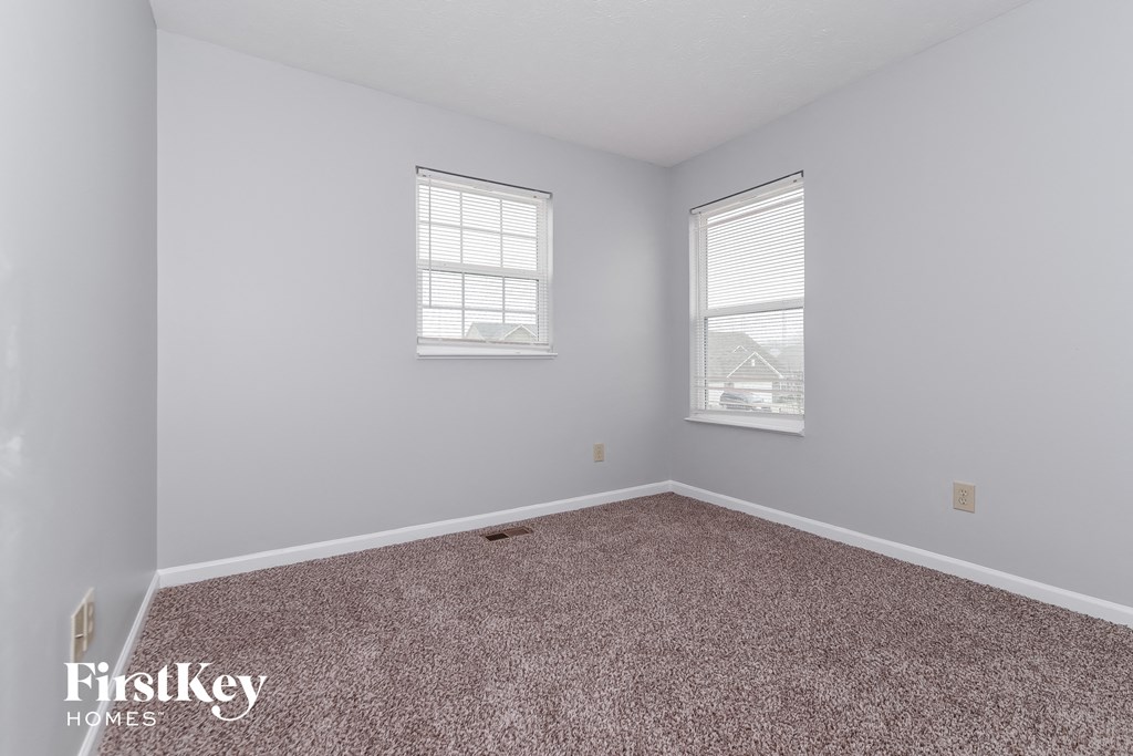 A room with a carpeted floor and two windows.