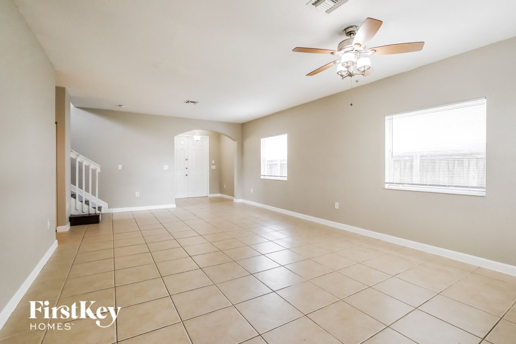 an empty living room with a ceiling fan and tiled floors