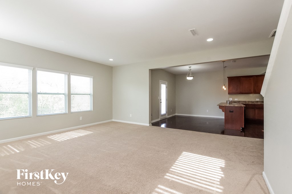 an empty living room with a kitchen in the background