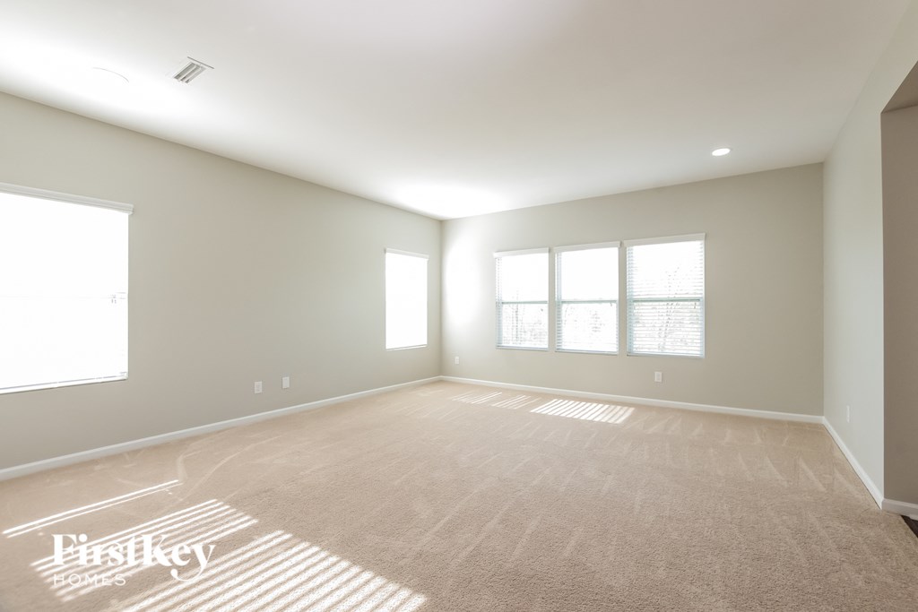 a spacious living room with a carpeted floor and three windows