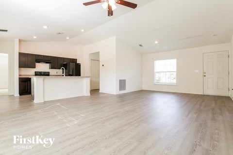 A spacious living room with a kitchen in the background and a ceiling fan above.