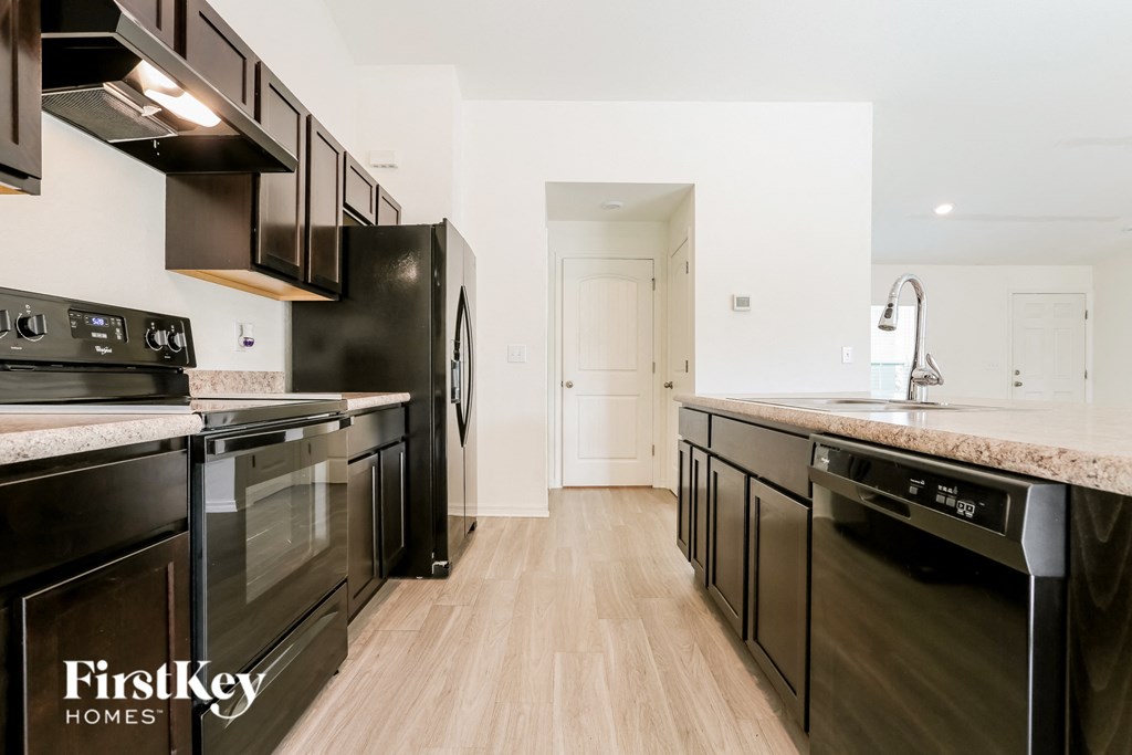 A kitchen with black appliances and wooden floors.