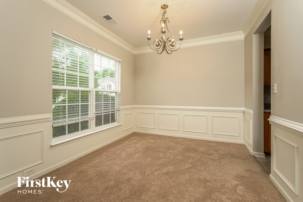 A room with a chandelier, a window with blinds, and a carpeted floor.