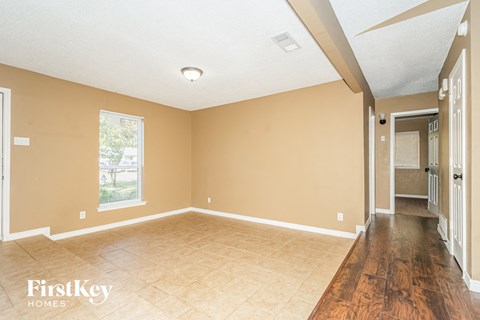 A room with beige walls and wooden flooring, with a window and a door visible.