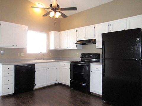 A black refrigerator is in a kitchen with white cabinets.