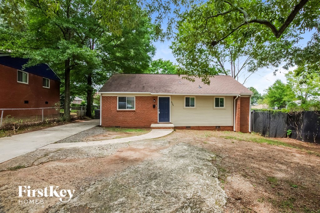 a small brick house with a gravel driveway and trees