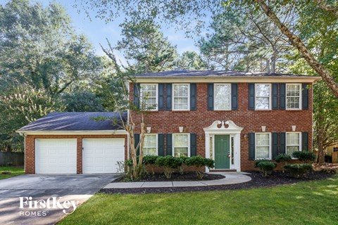 a brick house with a green door and white garage doors