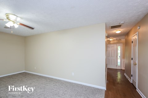 an empty living room with a ceiling fan and a door to a hallway