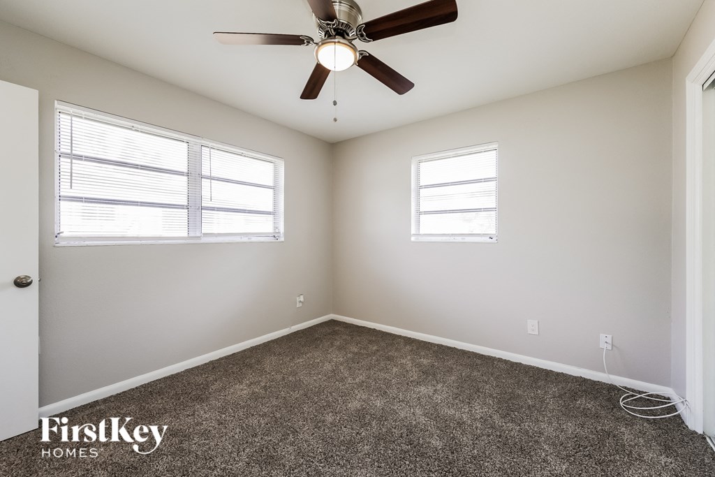 A room with a ceiling fan and two windows.