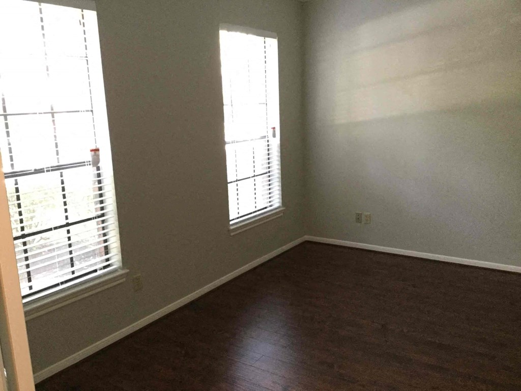 A room with wooden floors and two windows with blinds.