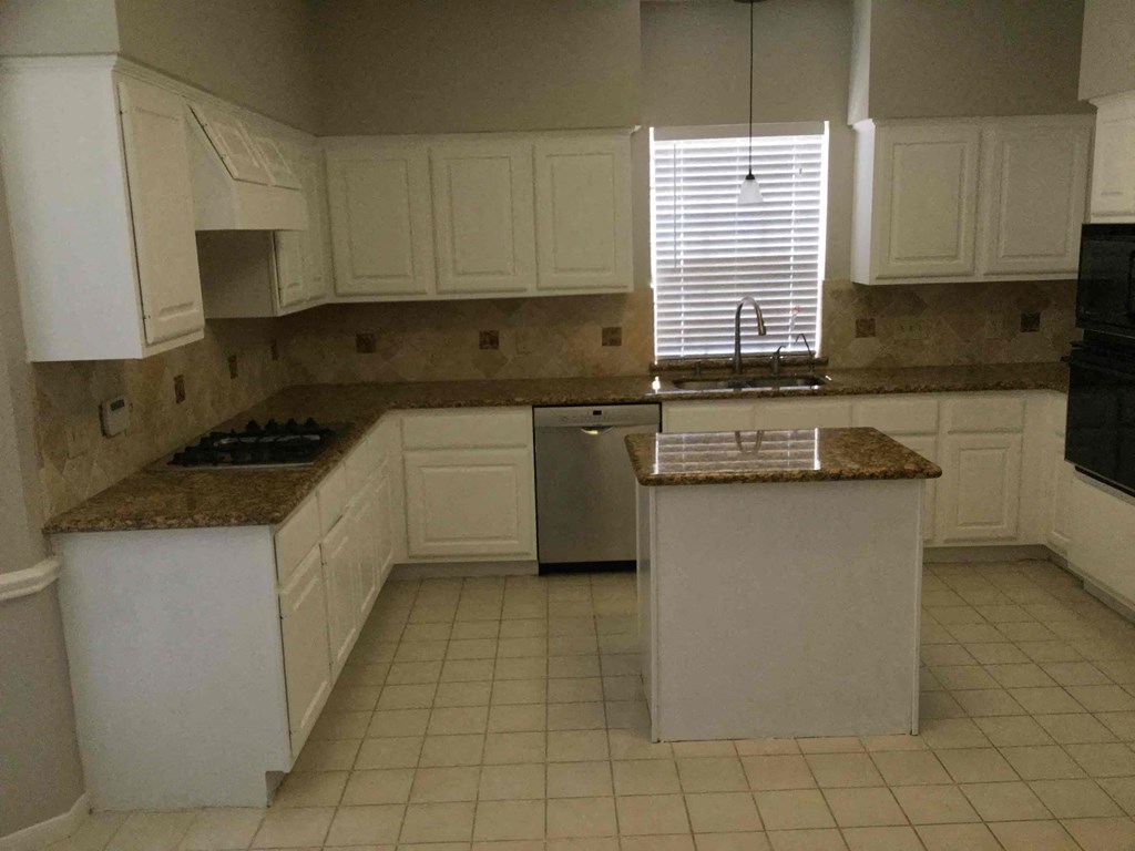 A kitchen with white cabinets and a granite counter.