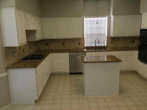 A kitchen with white cabinets and a granite counter.