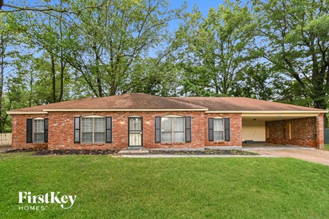 front view of a brick house with a lawn and trees